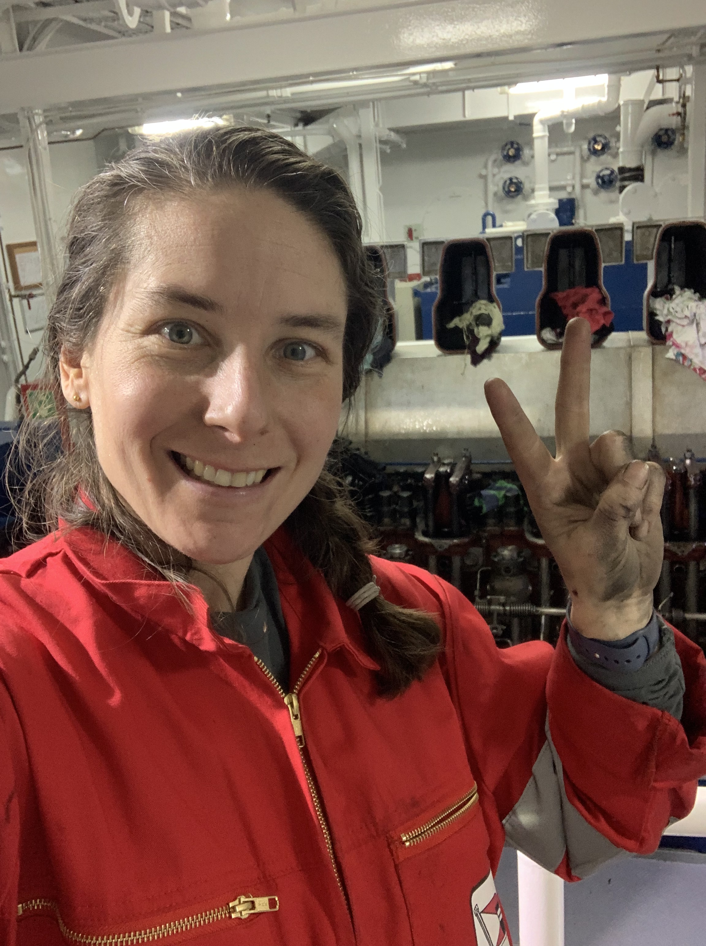Chief officer Sophie happy in her overall in the engine room making a peace sign with her hand